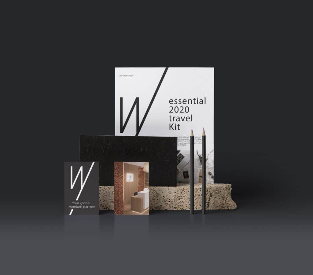 Stationary mockup with a black/grey background. W Premium group magazine standing on end with an A4 folder in front. 2 business cards on end in front. 2 pencils on end on the right. Elegant and balanced scene