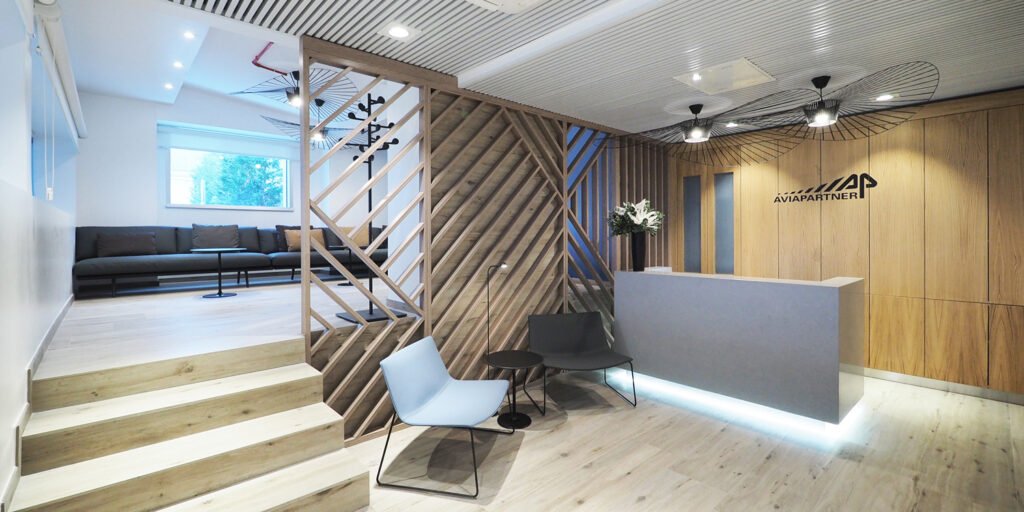 Aviapartner executive lounge reception at Rome Ciampino with a lit grey desk, diagonal timber screen and raised sofa area.