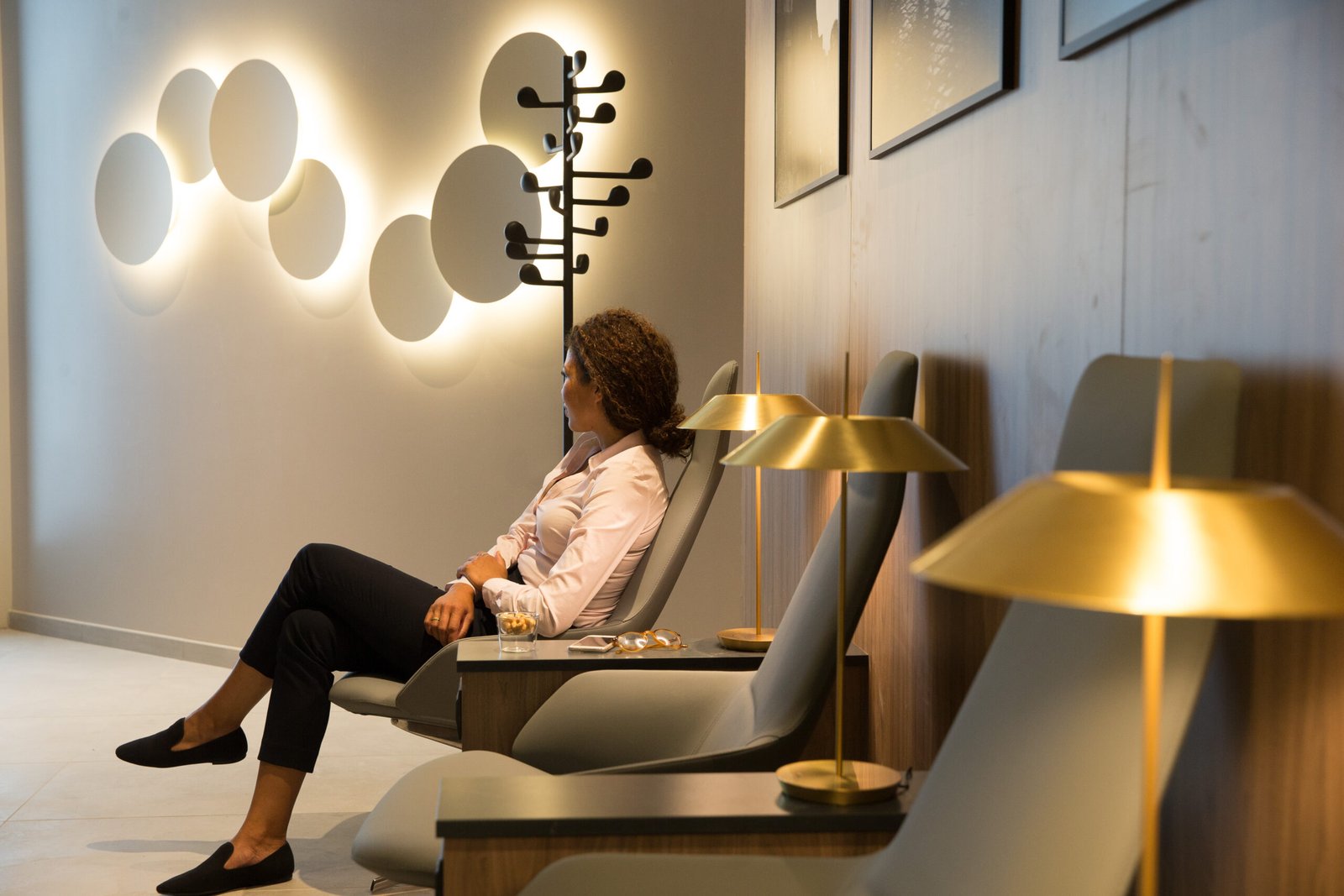 A guest relaxes in an upholstered lounge chair beside gold table lamps and illuminated circular wall features at the Star Alliance Lounge in Rome.