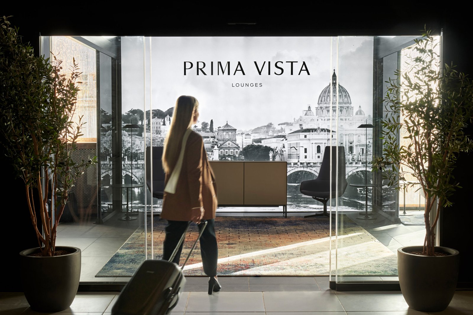 Traveler entering the Prima Vista Portus VIP lounge through glass doors at Rome Fiumicino Airport.
